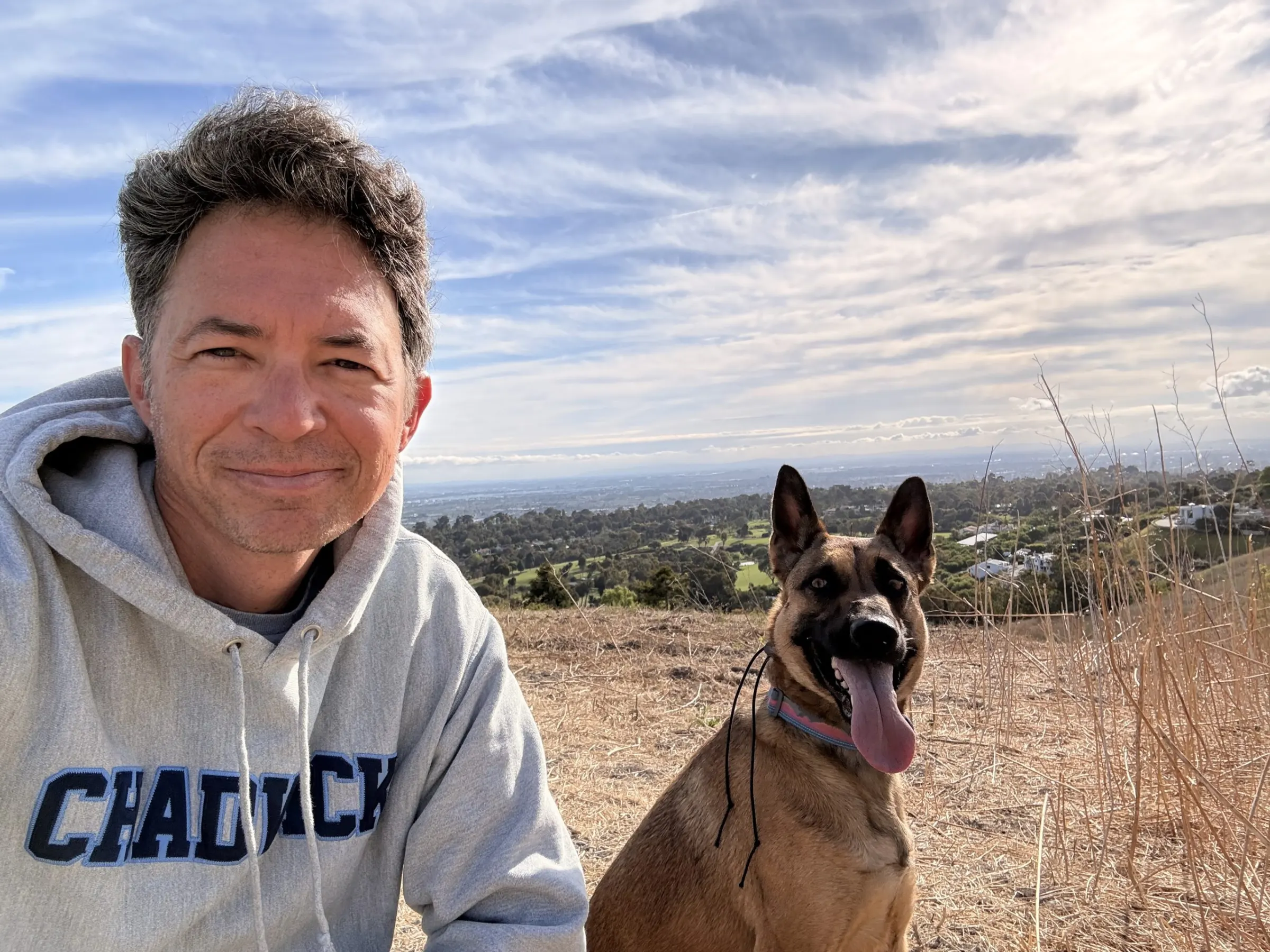 Mike, the owner of Palos Verdes K9, taking a picture with a dog sticking its tongue out. 